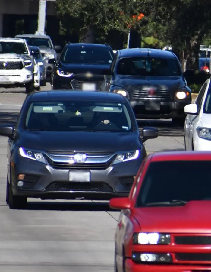 Line of cars in heavy traffic on a sunny street, front car approaching in foreground with other vehicles behind.