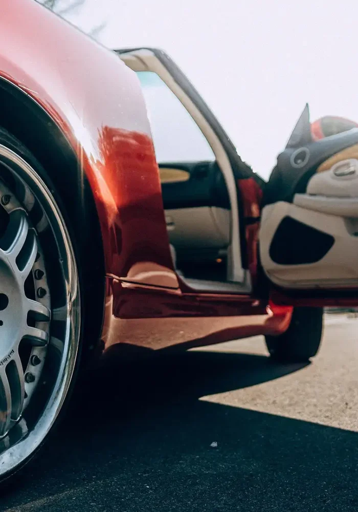 Low-angle view of a red sports car with its driver's door open, exposing a chrome alloy wheel.